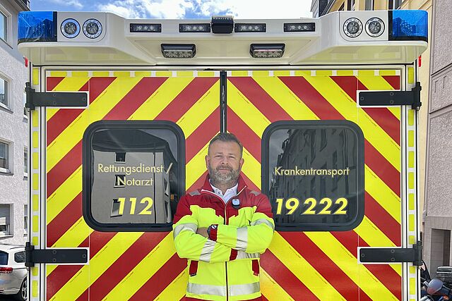 Rettungsdienstmitarbeiter in Dienstkleidung steht vor RTW