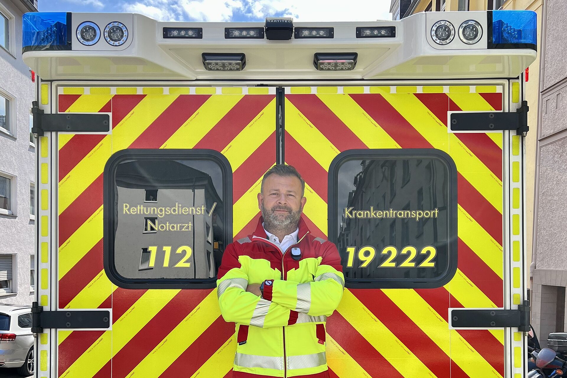Rettungsdienstmitarbeiter in Dienstkleidung steht vor RTW