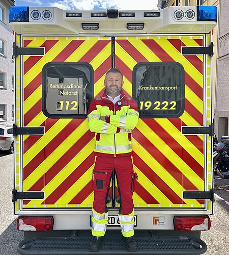 Rettungsdienstmitarbeiter in Dienstkleidung steht vor RTW